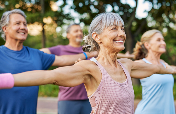 Adults over 50 practicing gentle, low-impact exercise outdoors with arms extended